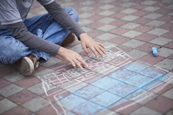 Hispanic boy typing on chalk laptop on sidewalk