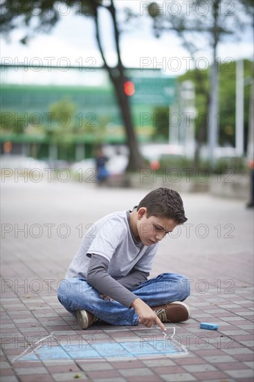 Hispanic boy drawing laptop with chalk on sidewalk