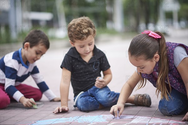 Hispanic boys and girl drawing with chalk on sidewalk