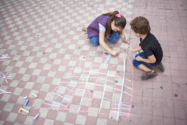 Hispanic boy and girl drawing with chalk on sidewalk