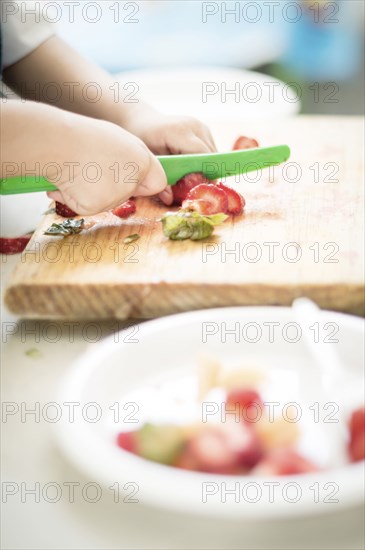 Hands of Hispanic boy cutting strawberry with plastic knife