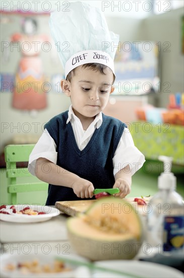 Hispanic boy cutting strawberry with plastic knife