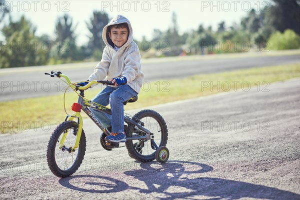 Hispanic boy posing on bicycle with training wheels