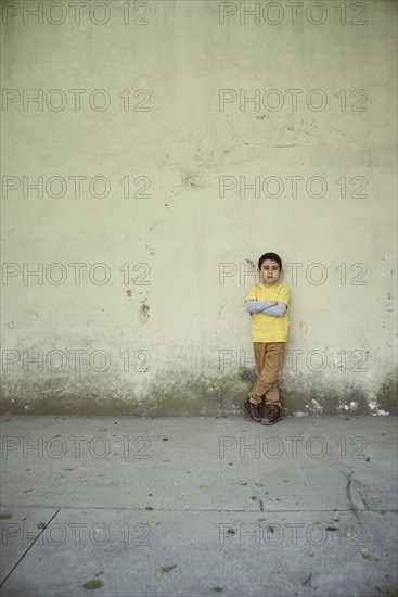 Serious Hispanic boy leaning on concrete wall