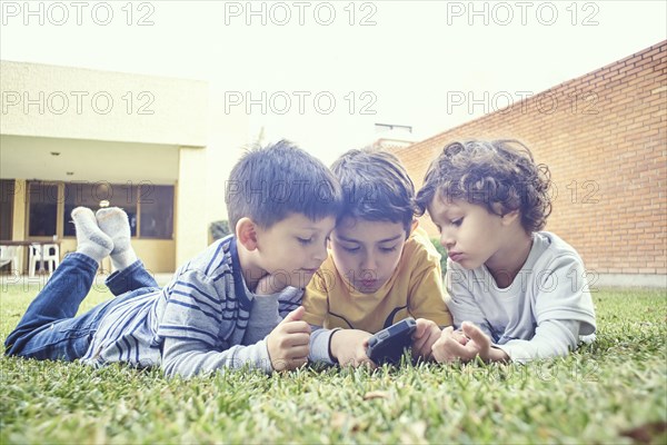 Hispanic boys laying in grass texting on cell phone
