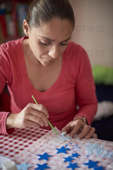 Hispanic woman painting stars at table