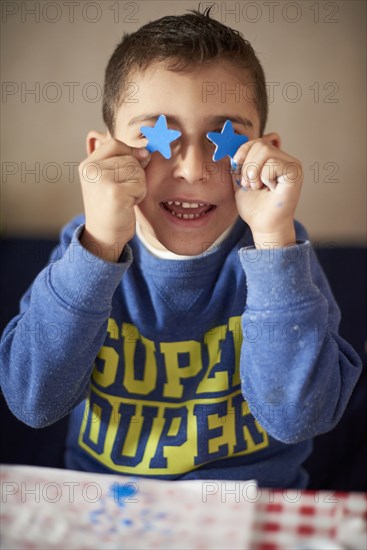 Hispanic boy covering eyes with blue stars at table