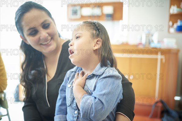 Hispanic mother watching daughter with Down Syndrome pointing to neck