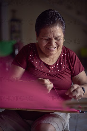 Hispanic woman weaving fabric on loom