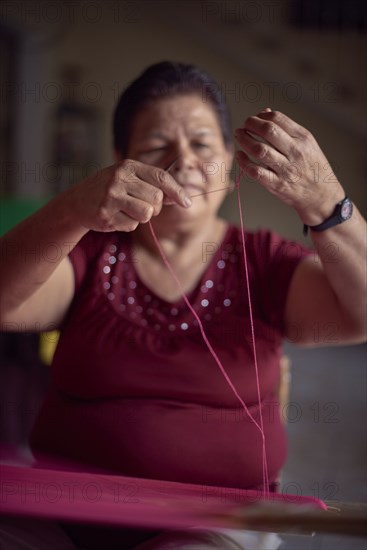 Hispanic woman weaving fabric on loom