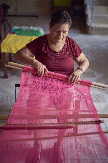 Hispanic woman weaving fabric on loom