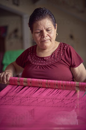 Hispanic woman weaving fabric on loom