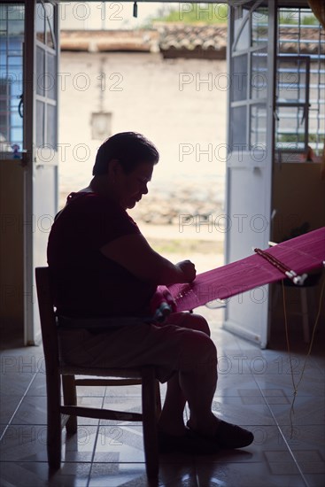 Hispanic woman weaving fabric on loom near doorway