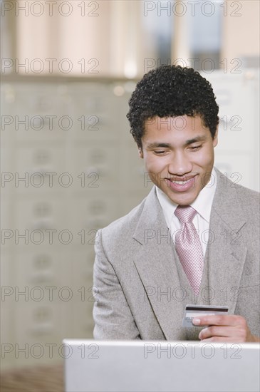 Mixed race businessman with laptop holding credit card