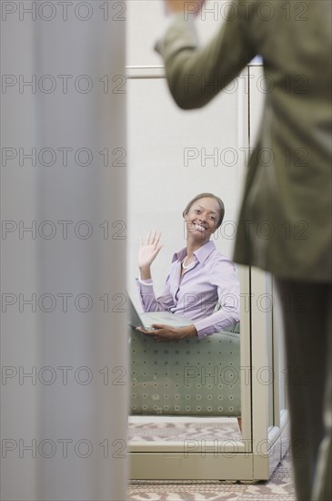 African businesswoman waving at co-worker in office