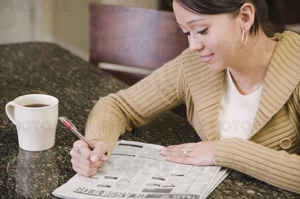 Hispanic woman searching newspaper classified ads