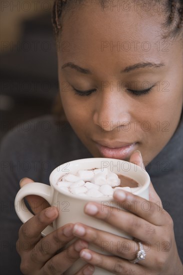 African woman smelling cup of hot cocoa with marshmallows