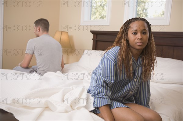 Multi-ethnic couple sitting at opposite edges of bed