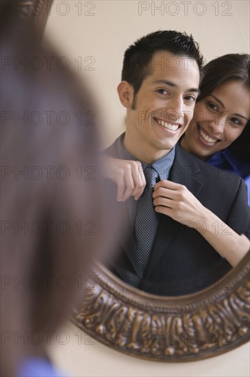 Hispanic woman helping husband with necktie