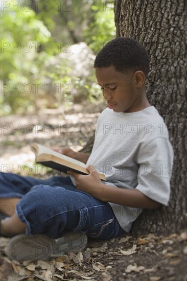 African boy reading book against tree