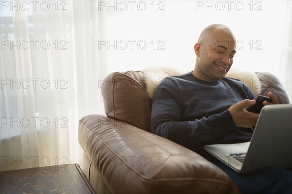 Mixed race man with laptop using cell phone