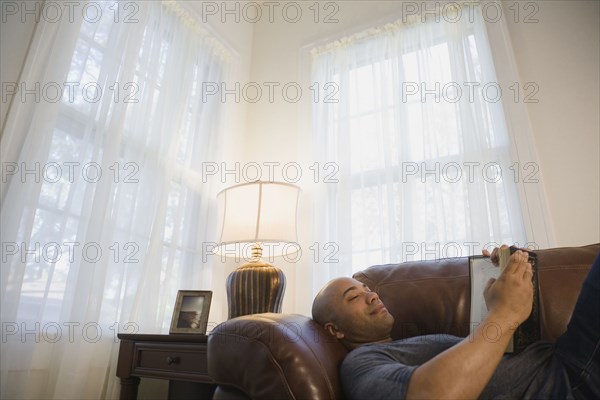 Mixed race man laying on sofa reading book