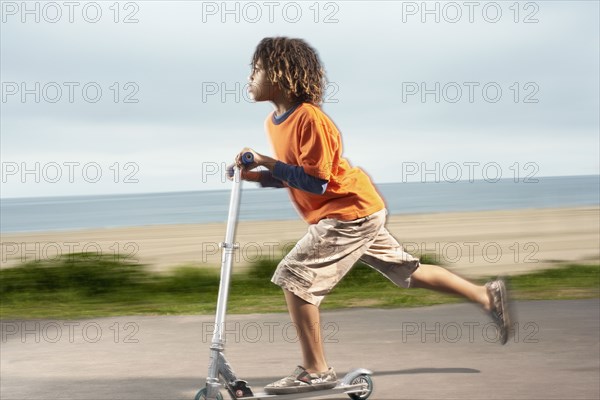 Mixed Race boy riding foot-powered scooter