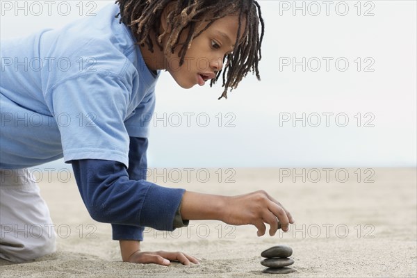 Mixed Race boy stacking stones on sand