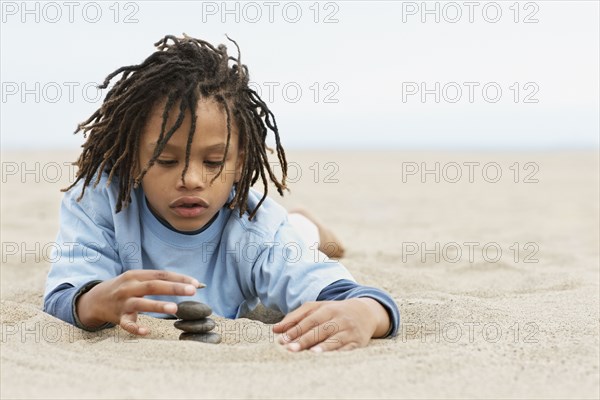 Mixed Race boy stacking stones on sand