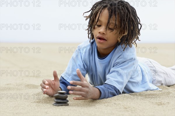 Mixed Race boy stacking stones on sand