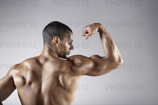 Bare chested mixed race man flexing biceps