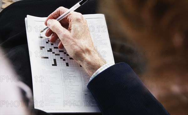 Close up of senior man's hand with pen on crossword puzzle