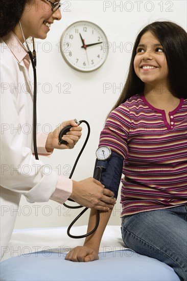 Female doctor taking young female patient's blood pressure