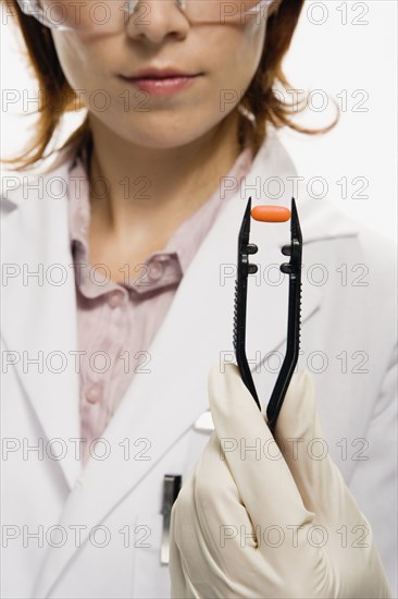 Female lab technician holding pill in large tweezers