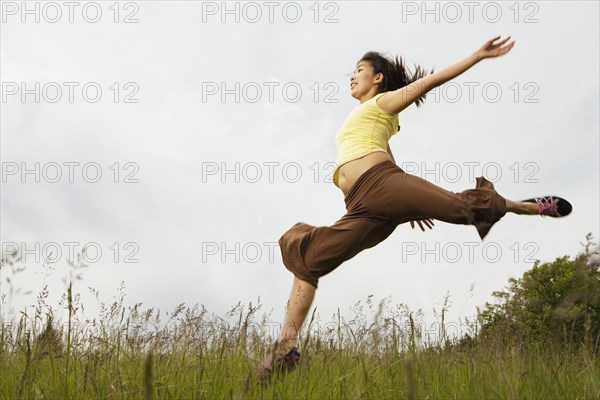 Asian woman jumping in meadow