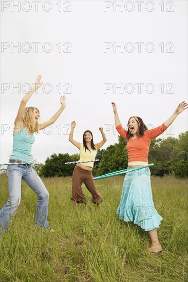 Three young women playing with plastic hoops in meadow