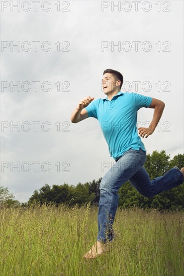 Young man running barefoot in meadow