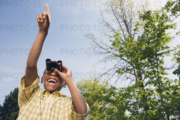 African boy using binoculars and pointing in park