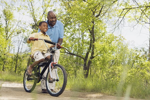 African grandfather teaching grandson to ride a bicycle in park