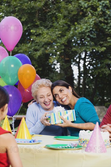 Senior Hispanic woman receiving gift at birthday party