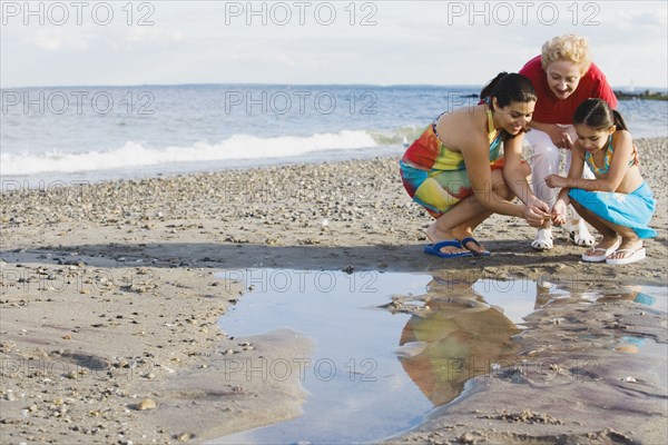 Hispanic grandmother mother and daughter looking in tide pool at beach