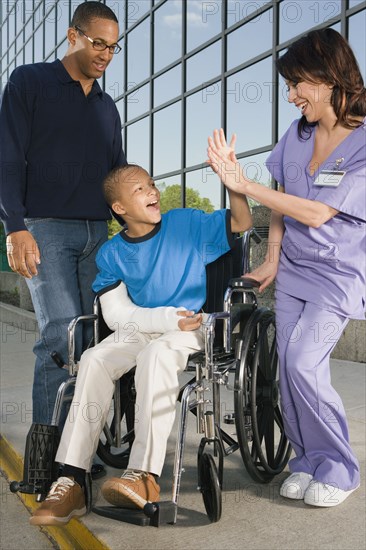 African boy in wheelchair high-fiving nurse in front of hospital