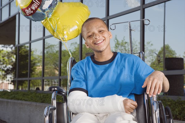 African boy with broken arm and balloons in wheelchair