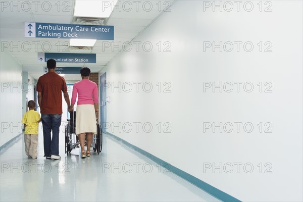 Rear view of African family walking down hospital corridor with wheelchair