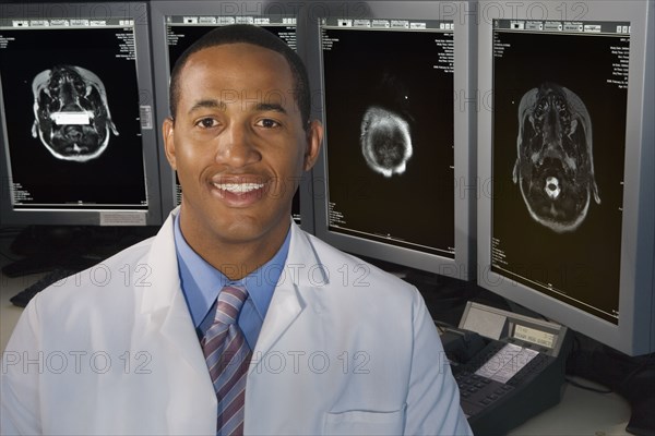 African male doctor smiling in front of brain scans
