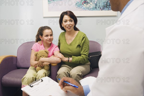 Doctor talking to Hispanic mother and daughter in waiting room