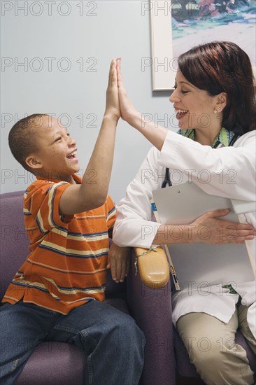 African boy and Hispanic female doctor high-fiving in waiting room