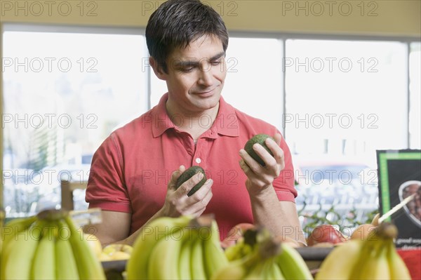 Man choosing avocados at grocery store
