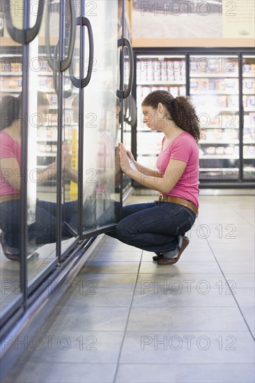 Mixed Race woman looking in freezer at grocery store