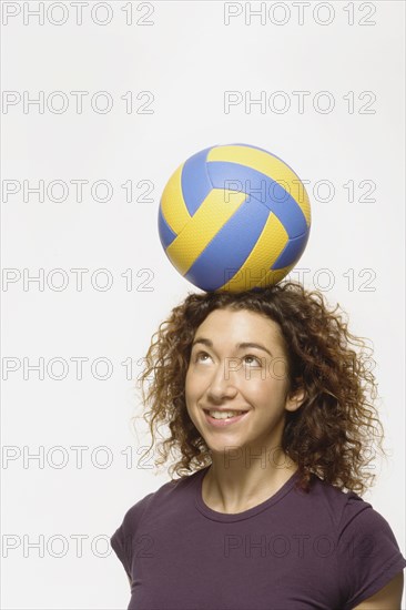 Mixed Race woman balancing volleyball on head